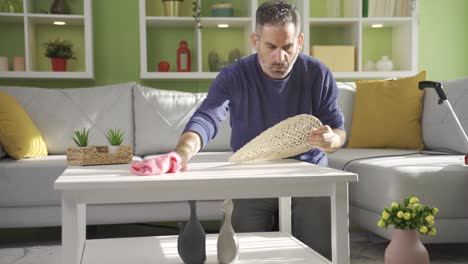 Mature-man-cleaning-at-home,-wiping-furniture-with-cloth-in-living-room.